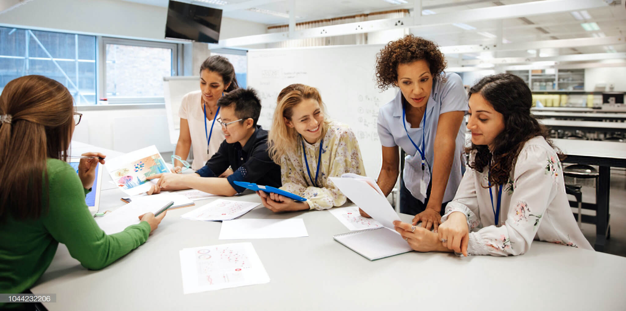 Group of people reviewing documents at a white table in a lab setting.